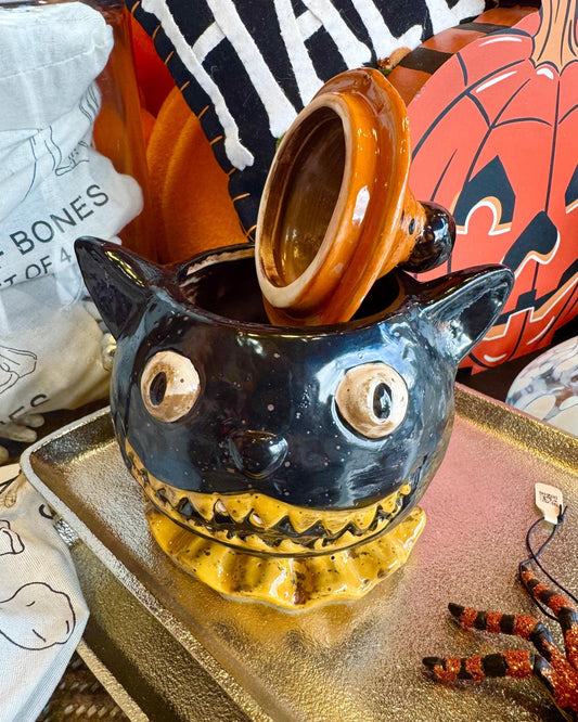 A ceramic Halloween lidded jar shaped like a black cat wearing an orange witch hat.