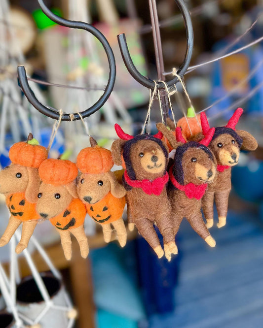 A group of small felt animal ornaments hanging from black hooks, including brown deer with red necklaces and pumpkins in orange with black jack-o'-lantern faces.