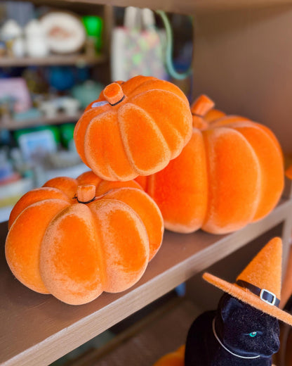 Three plush orange pumpkins displayed on a wooden shelf.