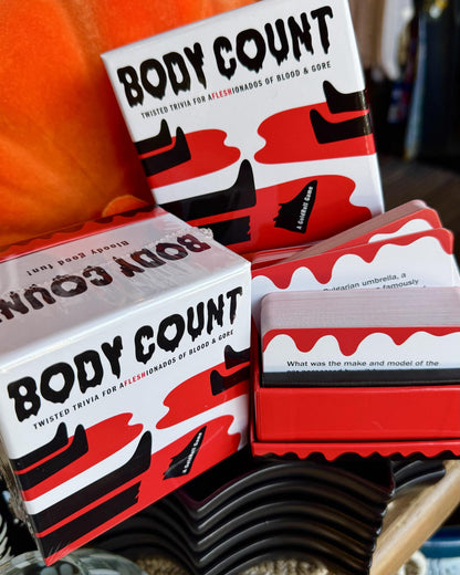 Body Count trivia game set with white boxes featuring red and black abstract graphics, red card sleeves, and cards stacked in a display stand.