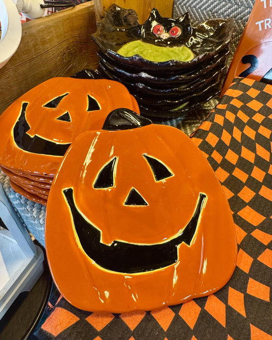 Orange ceramic jack-o'-lantern plates with black faces, shown with stacks of matching plates.