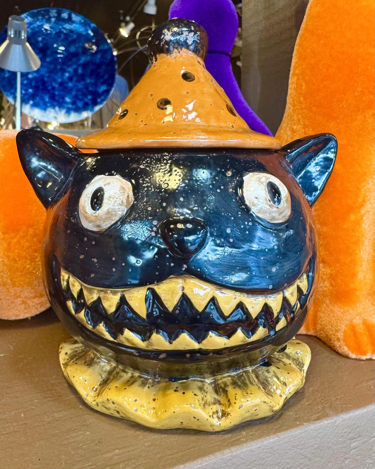 A ceramic Halloween lidded jar shaped like a black cat wearing an orange witch hat.