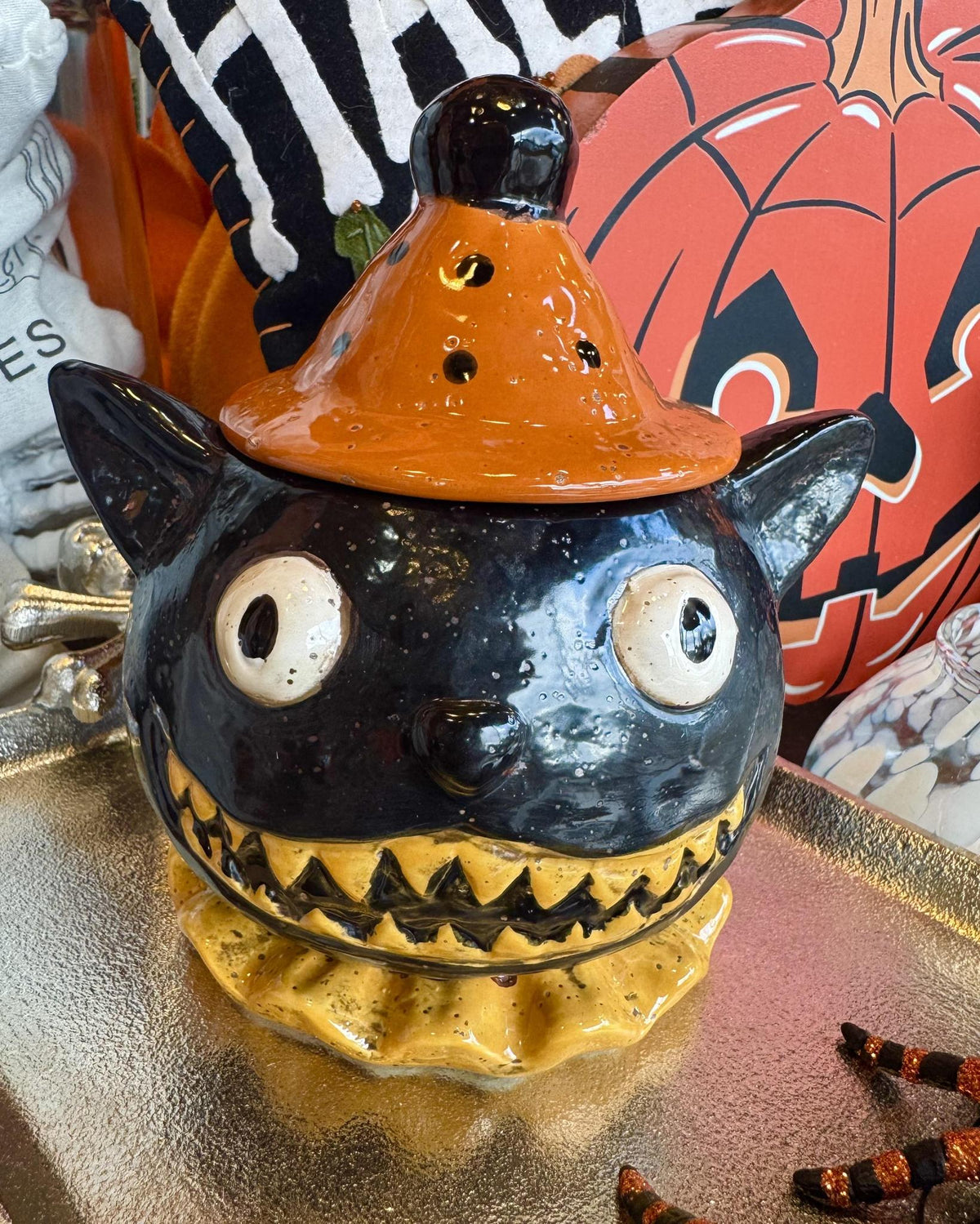 A ceramic Halloween lidded jar shaped like a black cat wearing an orange witch hat.